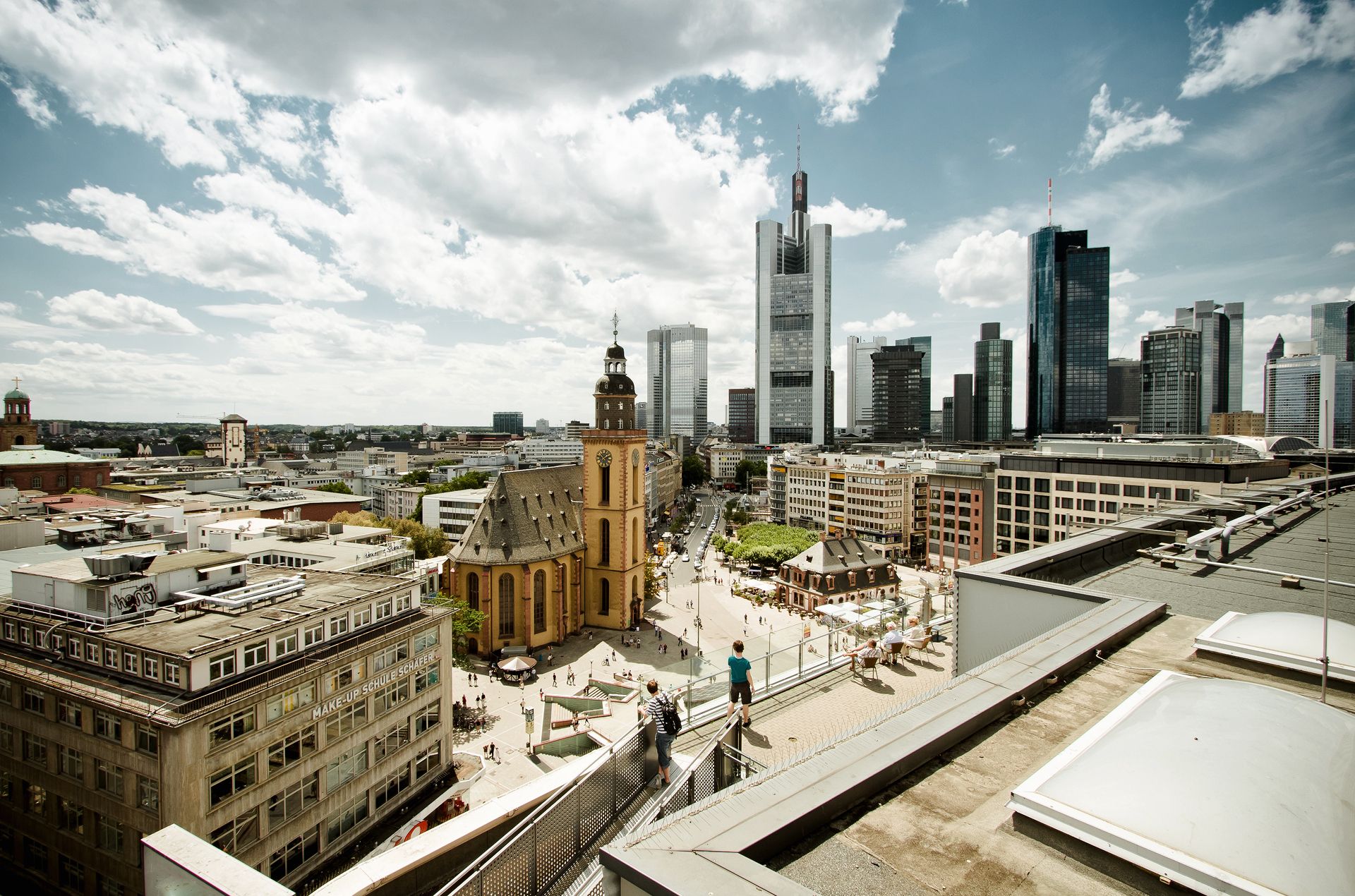 Skyline von Frankfurt mit Kirchturm, modernen Hochhäusern und belebtem Platz